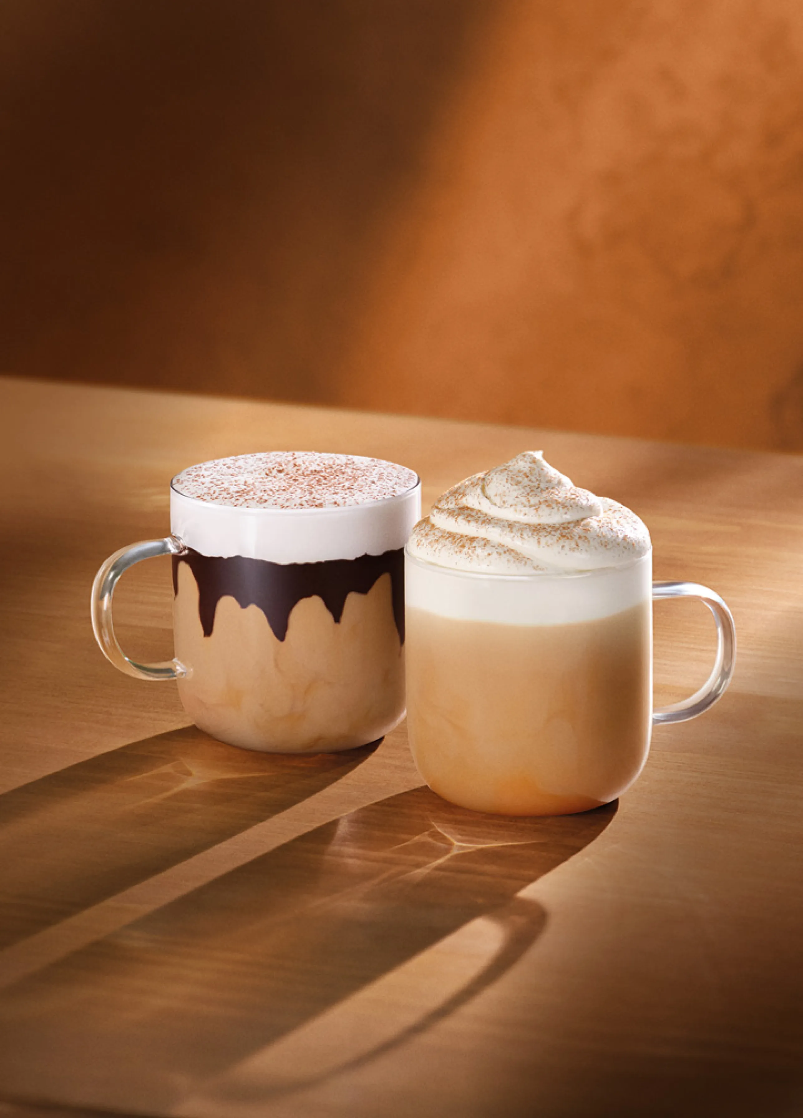 Dos cafés calientes, un Pumpkin Spice Latte y un Tiramisú Velvet Latte, sobre una mesa de madera con tonos otoñales 