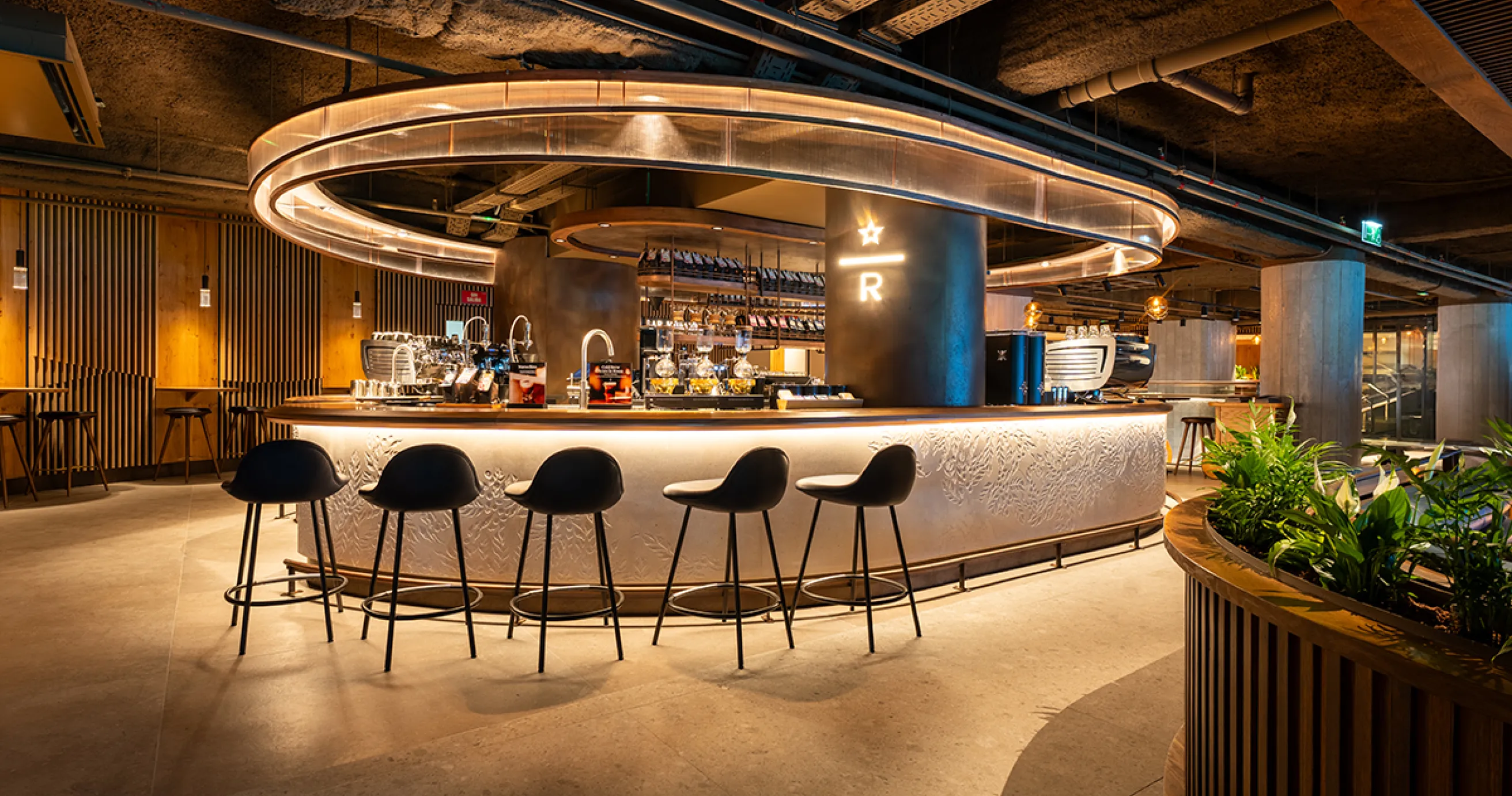 Imagen de la barra Mixato y Reserve de Starbucks Bernabeu, se ve iluminada, con cinco sillas negras