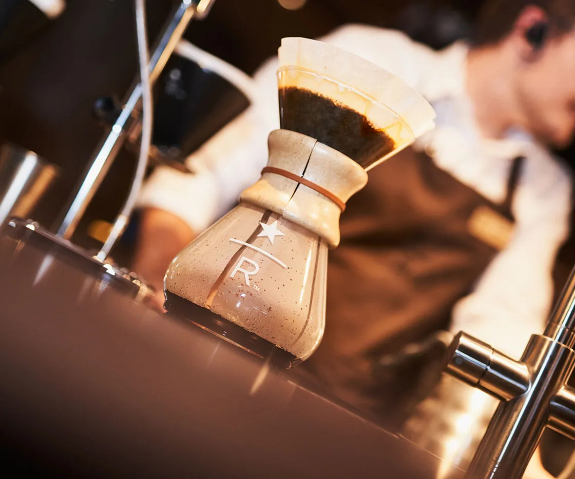 Imagen de cafetera de filtro donde se ve el logo de Starbucks Reserve. De fondo se ve a un barista