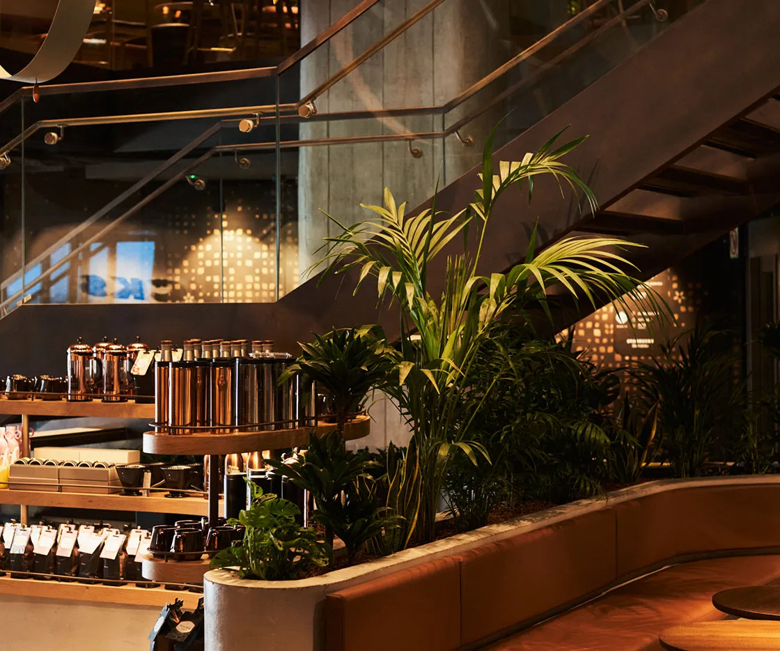 En la foto se ve el mueble de merchandising con asientos de madera y una planta. De fondo se ven las escaleras