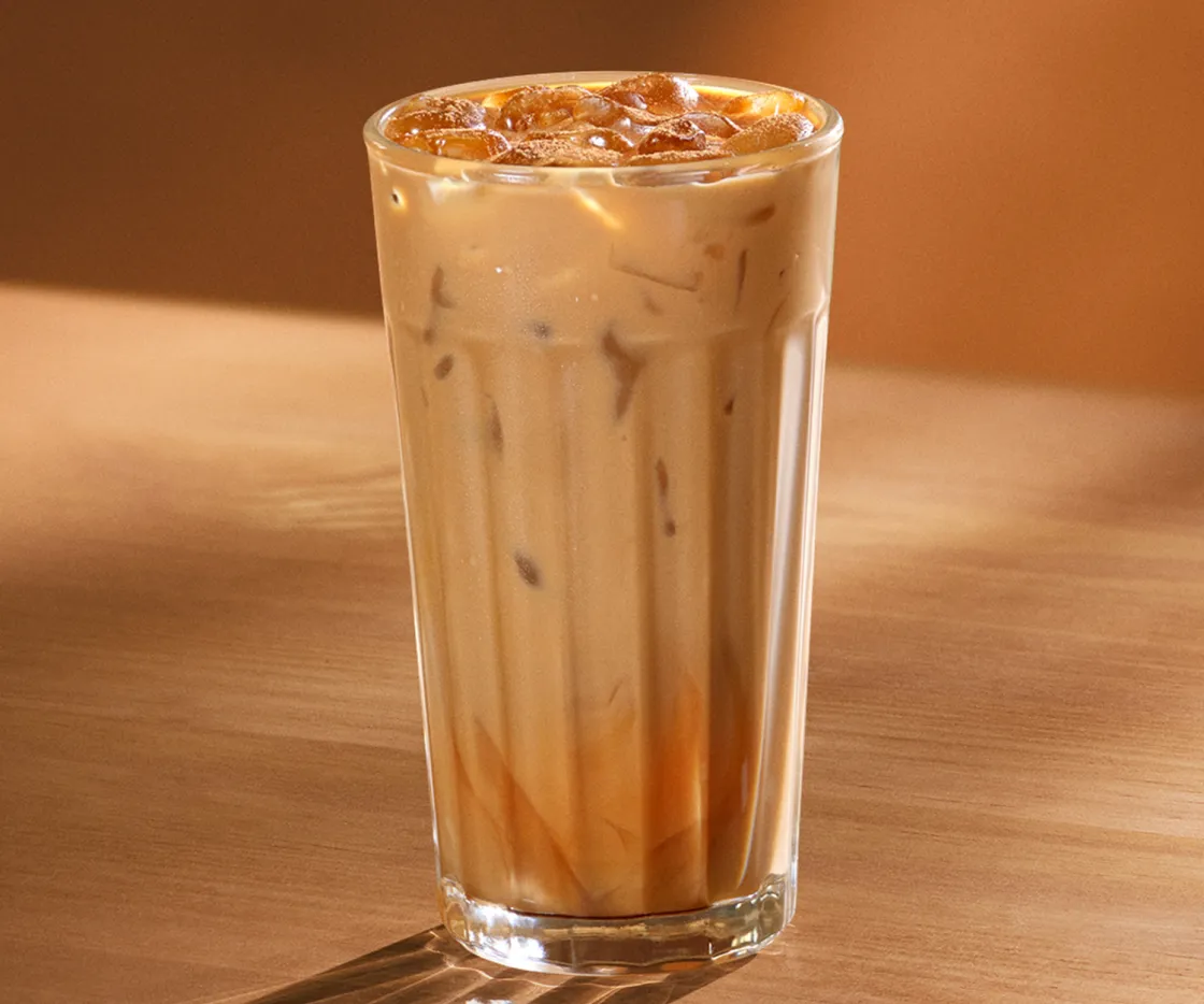 Vaso de Pumpkin Spice Latte frío, sobre una mesa de madera con tonos otoñales