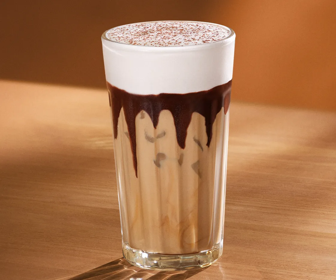 Vaso de Tiramisú Velvet Latte frío, sobre una mesa de madera con tonos otoñales