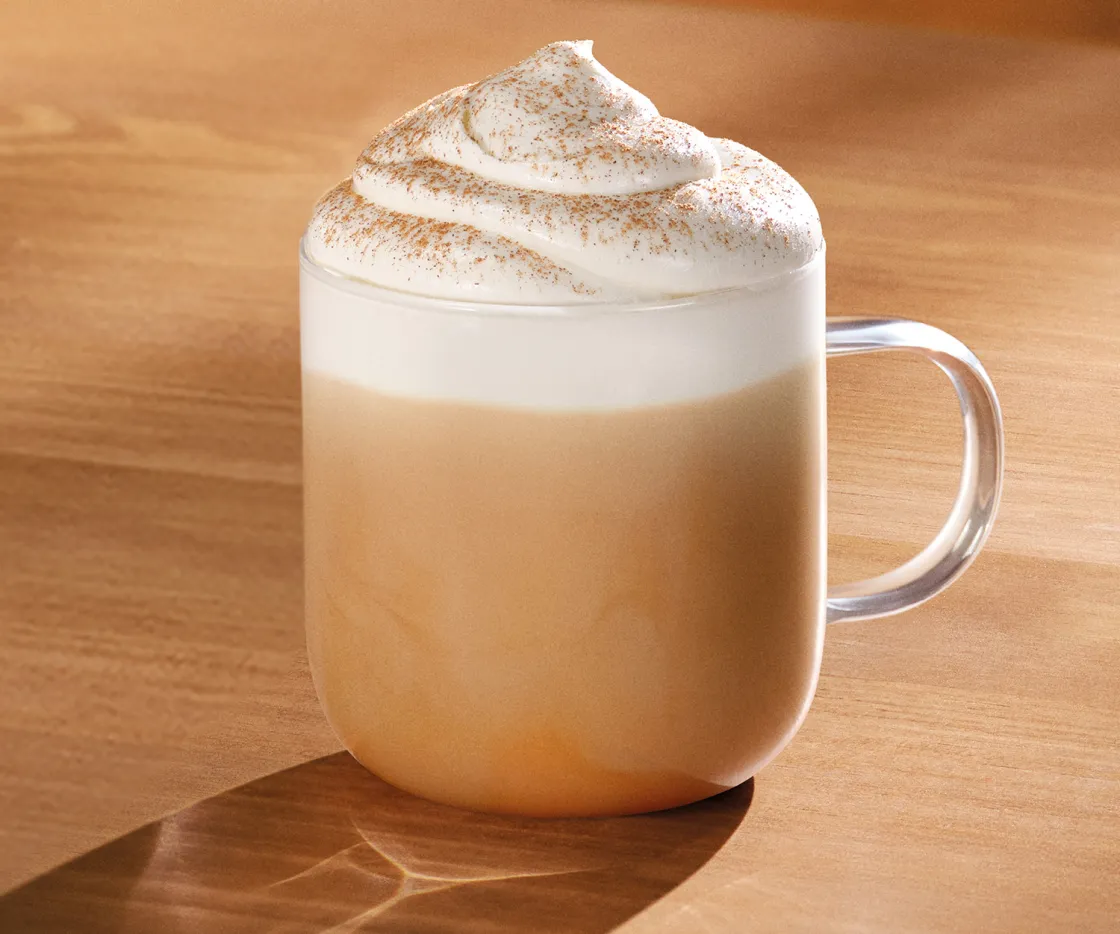 Taza de Pumpkin Spice Latte caliente, sobre una mesa de madera con tonos otoñales