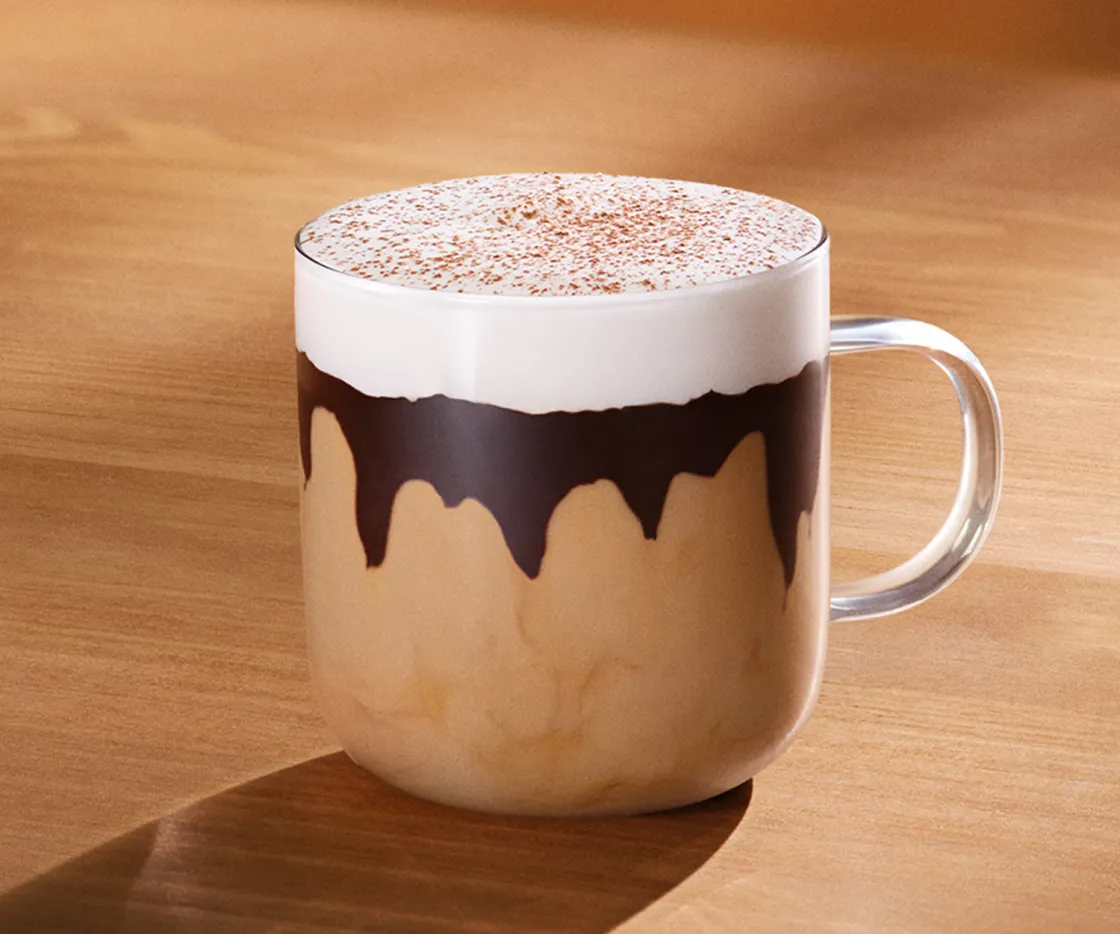 Taza de Tiramisú Velvet Latte caliente, sobre una mesa de madera con tonos otoñales