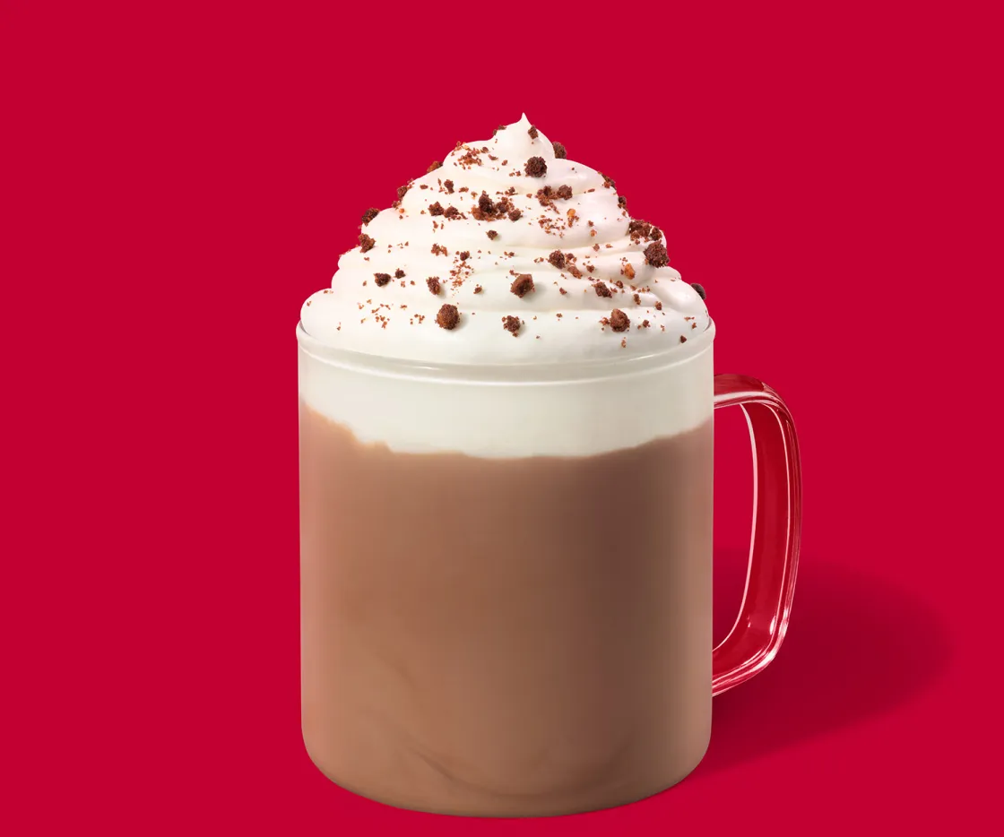 Fudge Brownie Hot Chocolate caliente con nata en una tasa de vidrio, sobre un fondo rojo