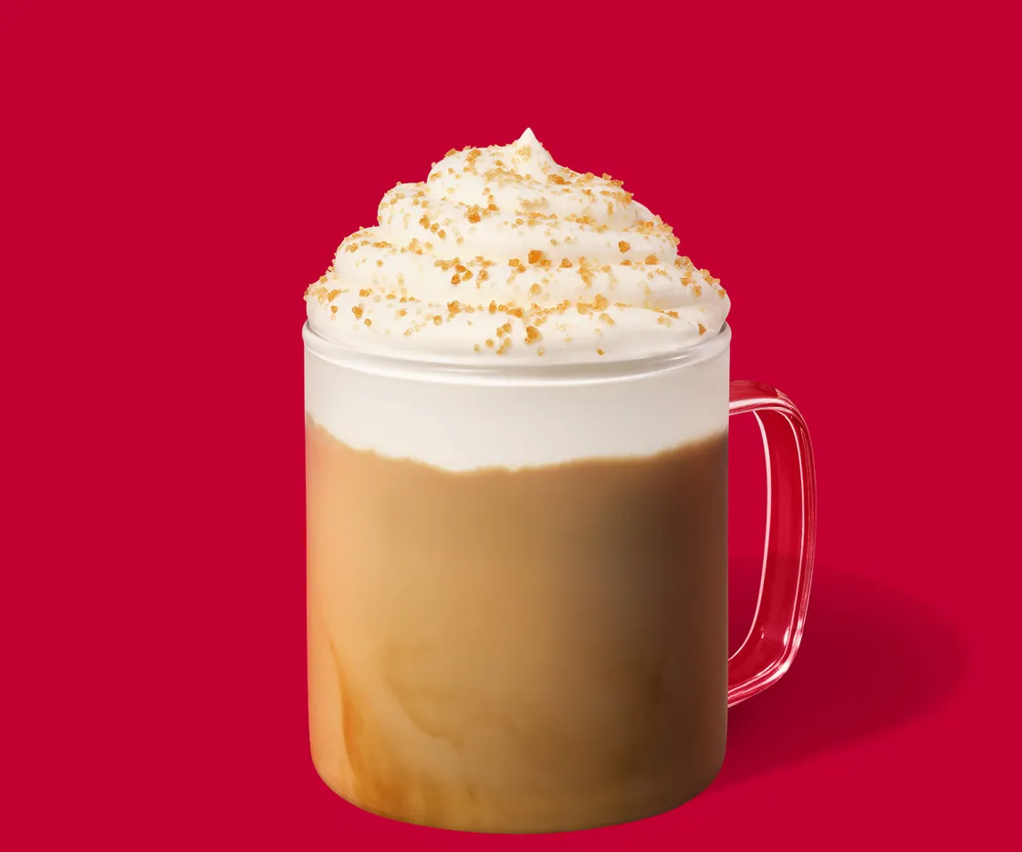 Toffee Nut latte caliente con nata en una taza de vidrio sobre un fondo rojo