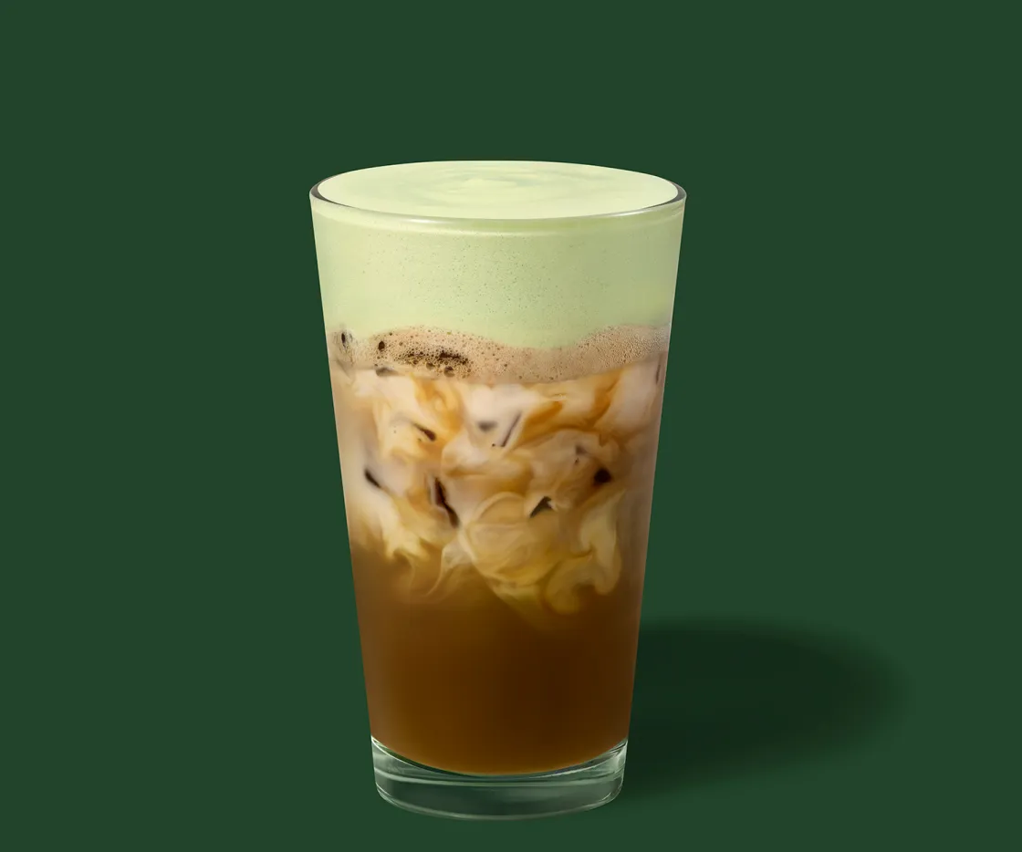 Un Iced Pistacho Avena Shaken Espresso en un vaso de vidrio con fondo verde