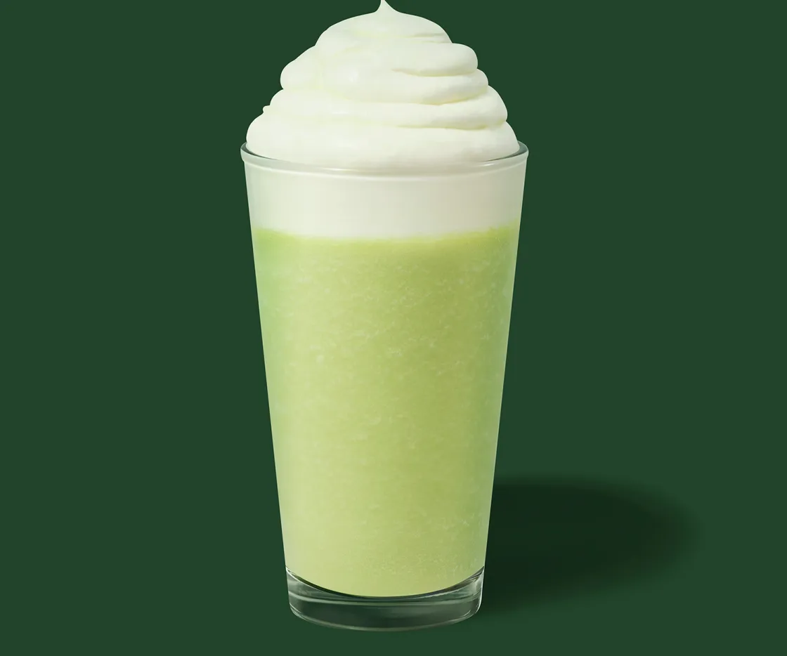 Un Frappuccino de Pistacho con nata en un vaso de vidrio con fondo verde