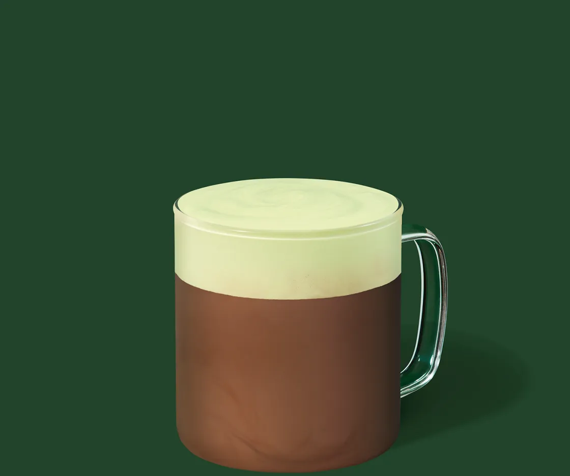 Un Pistacho Hot Chocolate en una taza de vidrio con fondo verde