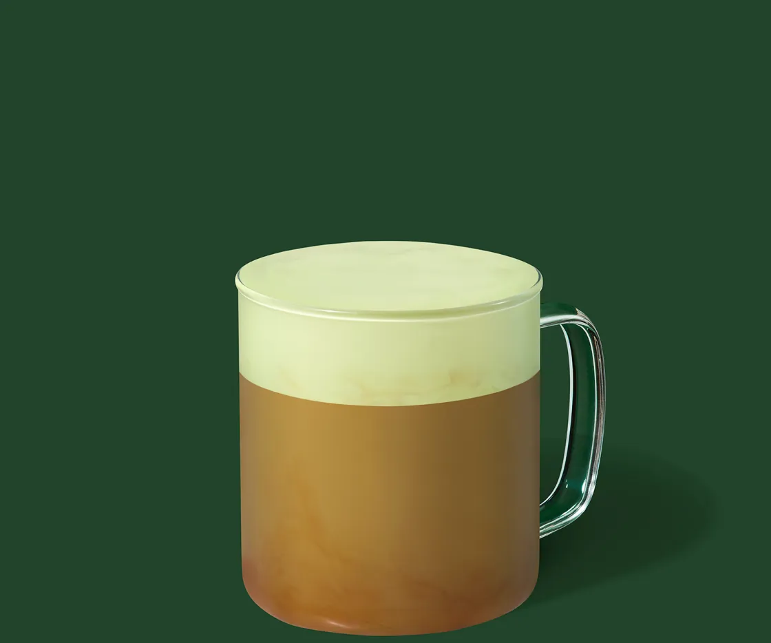 Un pistacho velvet latte caliente en una taza de vidrio con fondo verde