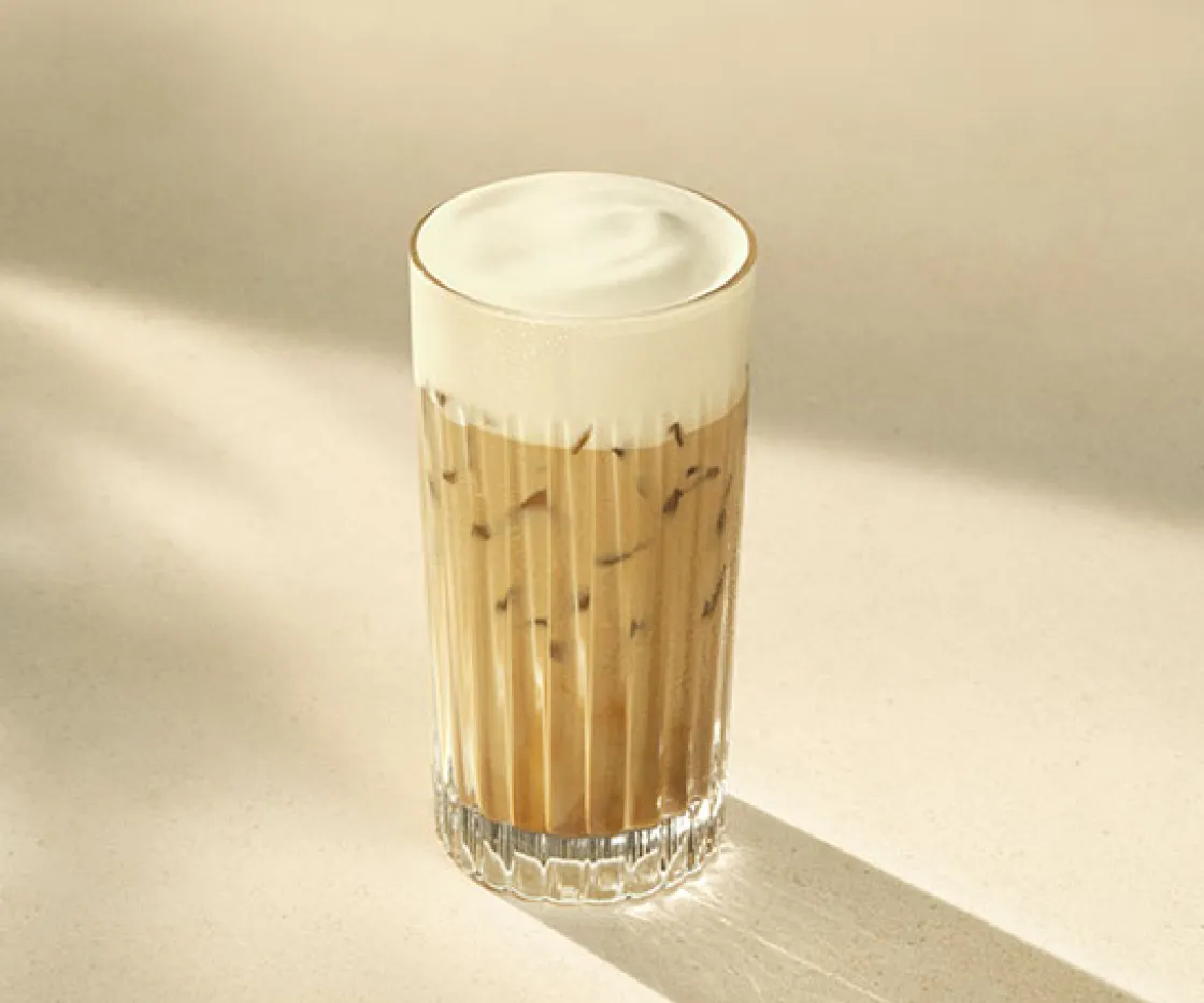 Imagen de un vaso de cristal, dentro tiene un café latte iced con espuma de proteina