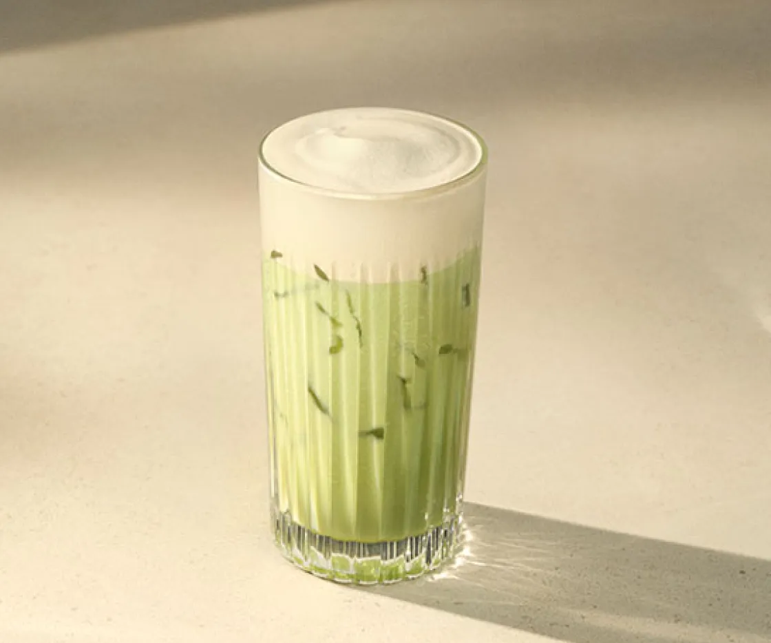 Imagen de un vaso de cristal, dentro tiene un te matcha iced con espuma de proteina