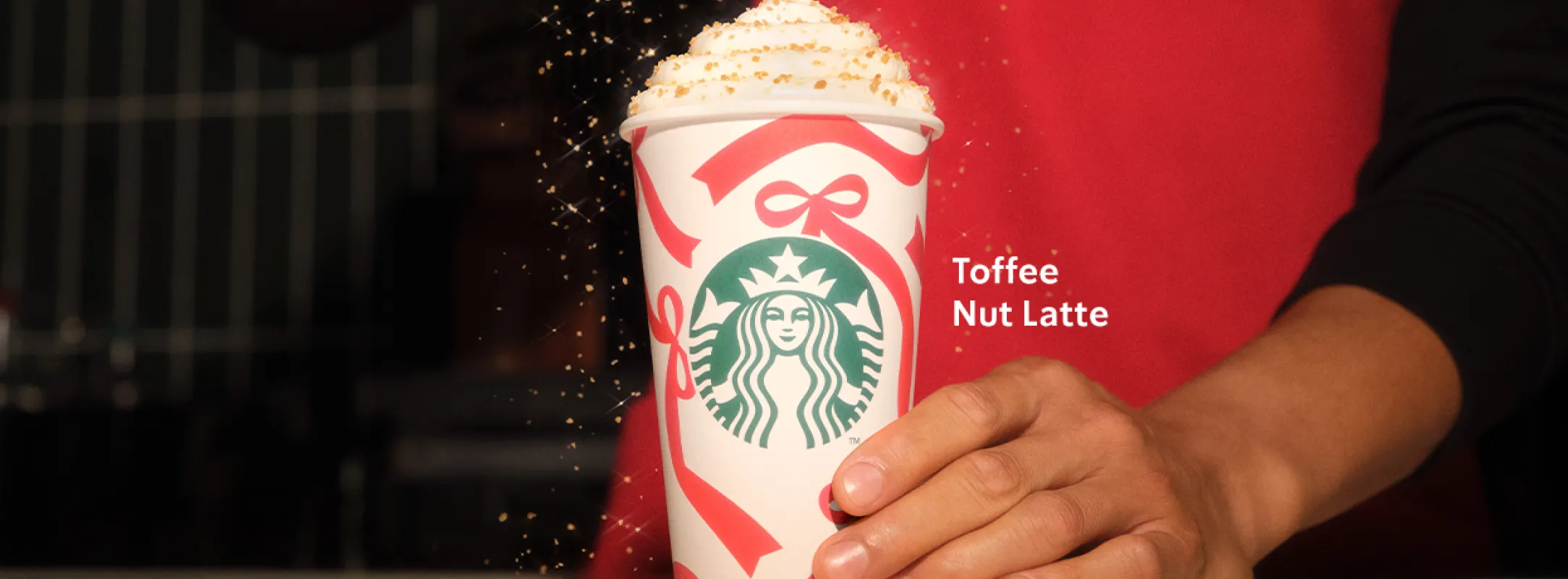 Imagen centrada de un Toffee Nut latte siento terminado por un barista con un delantal rojo