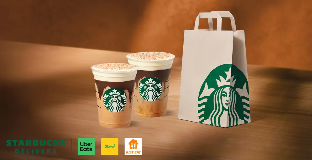 Dos cafés y una bolsa para llevar, sobre una mesa de madera con tonos otoñales 